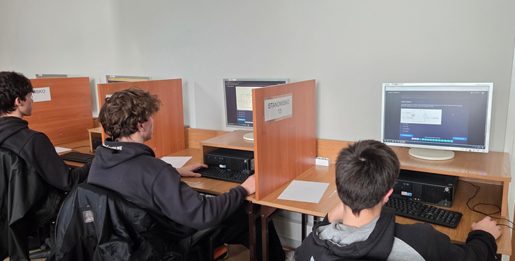 Zdjęcie przedstawia uczestników Olimpiady Wiedzy Elektrycznej „ElektroChallenge”, którzy w skupieniu rozwiązują zadania przy komputerowych stanowiskach konkursowych