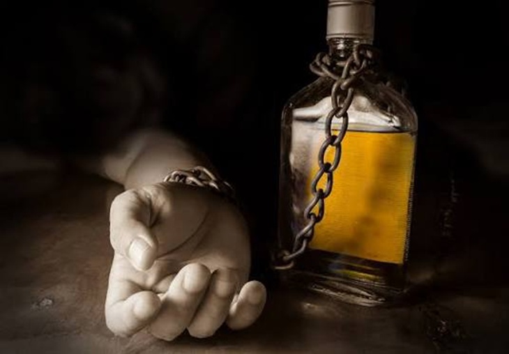 Na zdjęciu widoczna jest butelka alkoholu opleciona metalowym łańcuchem, symbolizująca uzależnienie i poczucie zniewolenia. Obok znajduje się dłoń zaciśnięta w pięść, co może sugerować bezsilność, cierpienie oraz trudną walkę z nałogiem. Ciemne, stonowane tło oraz kontrast światła i cienia nadają fotografii poważny i niepokojący charakter. Zdjęcie w symboliczny sposób pokazuje, że uzależnienie od alkoholu może stać się pułapką, z której trudno się uwolnić.
