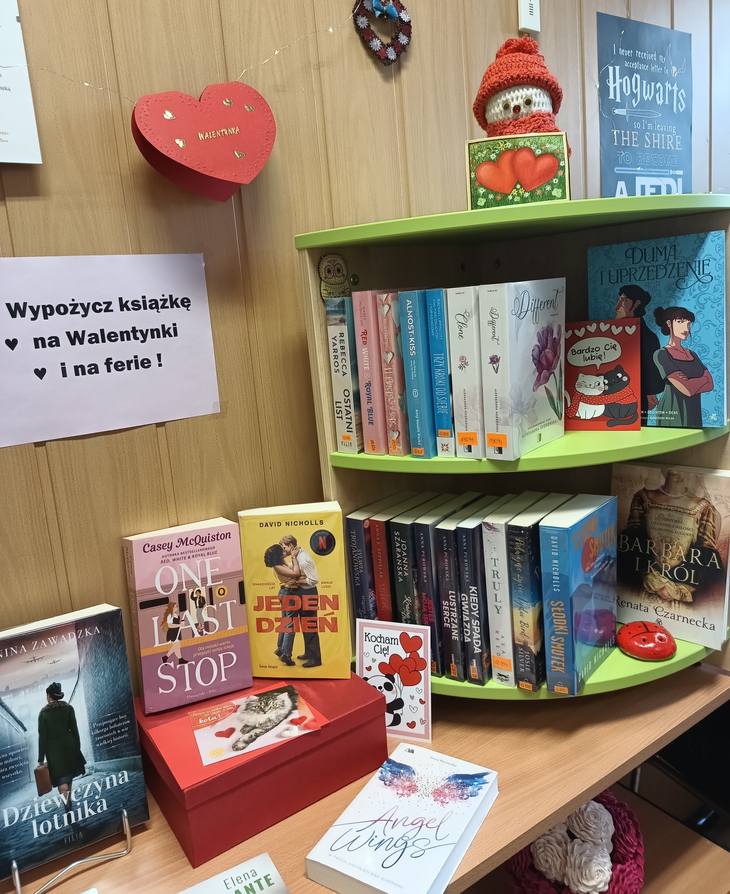 Półka z książkami i dekoracjami walentynkowymi w bibliotece, zachęcająca do wypożyczania lektur na Walentynki i ferie.