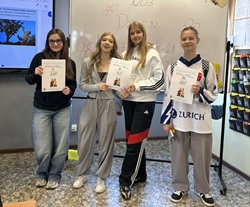 Na zdjęciu widać cztery uczennice stojące w klasie przed tablicą z napisem „Dzień Matematyki”. Trzy z nich trzymają dyplomy za zajęcie miejsc w konkursie matematycznym. Fotografia przedstawia moment wręczenia nagród i wspólnego świętowania sukcesów podczas szkolnych obchodów Dnia Matematyki.