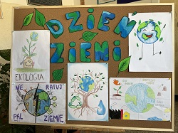Na zdjęciu widać tablicę korkową udekorowaną z okazji Dnia Ziemi. Znajdują się na niej kolorowe napisy „Dzień Ziemi”, rysunki planety, liści oraz prace uczniów przedstawiające tematykę ekologii i ochrony środowiska. Całość utrzymana jest w zielono-niebieskiej kolorystyce, podkreślającej troskę o naturę.