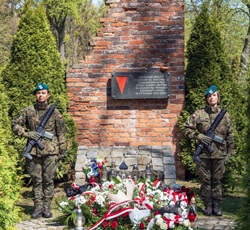 widoczny jest pomnik upamiętniający ofiary, przy którym stoją wartownicy honorowi. Pod pomnikiem złożono wieńce i kwiaty, co świadczy o pamięci i szacunku dla poległych.