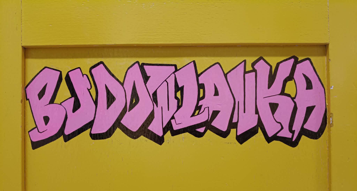 Kolorowy napis „Budowlanka” wykonany w stylu graffiti na żółtym tle – nowoczesny i młodzieżowy akcent nawiązujący do szkoły.