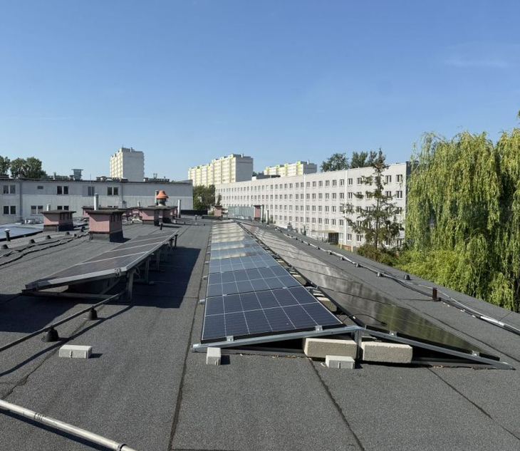 Na zdjęciu widoczna jest instalacja fotowoltaiczna zamontowana na dachu budynku szkoły. Moduły zostały rozmieszczone z uwzględnieniem odpowiedniego kąta nachylenia i warunków nasłonecznienia, co pozwala na efektywne pozyskiwanie energii ze słońca