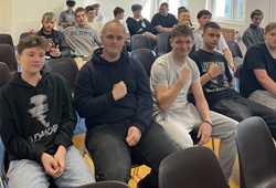 Na zdjęciu widać grupę uczniów siedzących w szkolnej sali. W pierwszym rzędzie kilku chłopaków pozuje do zdjęcia, część z nich pokazuje zaciśnięte pięści, jakby podkreślając ducha rywalizacji. W tle siedzą pozostali uczestnicy spotkania, którzy również przyglądają się wydarzeniu. Zdjęcie oddaje luźną, koleżeńską atmosferę i ducha wspólnej zabawy.